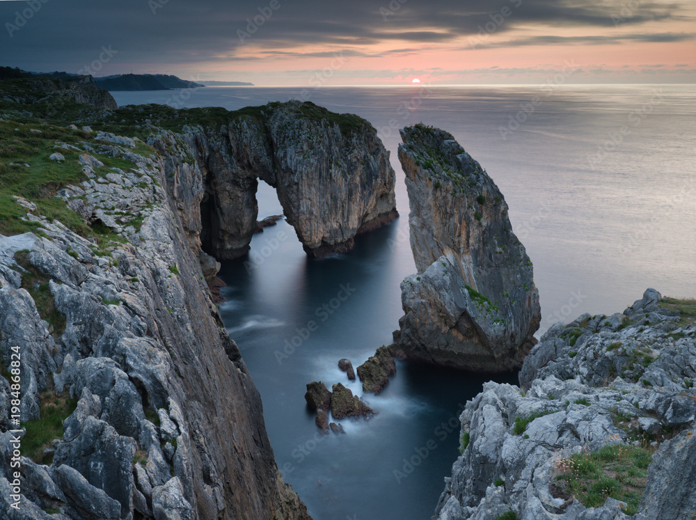 Fototapeta premium Epic Long Exposure Coastal Sea Arch at Sunset - Dramatic high-angle long exposure view of a massive natural sea arch and eroded cliffs framing the sunset over the Atlantic Ocean in Asturias.
