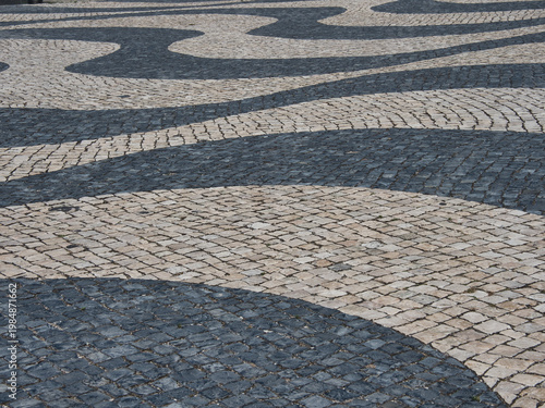 Traditional Portuguese Pavement Wave Pattern - Close-up abstract view of the iconic Calçada Portuguesa cobblestone pavement with a black and white wavy design.