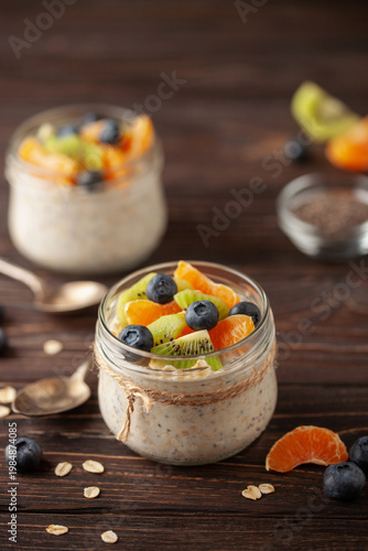 Healthy diet breakfast. Overnight oatmeal with chia seeds and fruits in a glass jar on a wooden background.