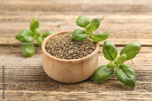 Dry basil in bowl and fresh leaves on wooden table, closeup