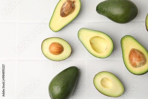 Whole and cut fresh avocados on white tiled table, flat lay. Space for text