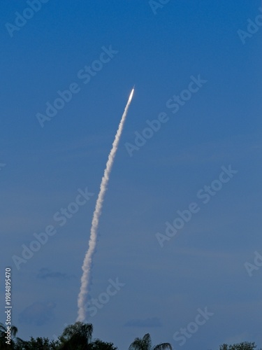April 1, 2026 Artemis II  rocket launch climbing above tree line with trailing thin bright contrail