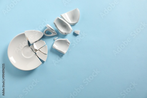 Foto Pieces of broken saucer on light blue background, flat lay