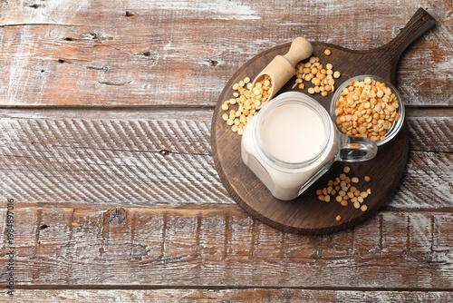 Fresh pea milk in mason jar and seeds on wooden table, top view with space for text. Vegan drink