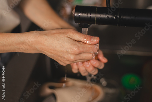 Close up of woman hands carefully washing a brown chicken egg under running water from a black faucet. Female cleaning fresh organic ingredients in kitchen sink for healthy meal preparation.
