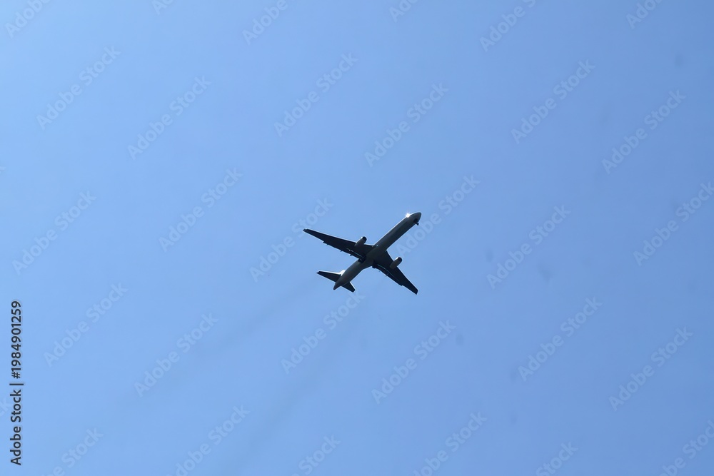 Fototapeta premium A commercial airplane flying high in the clear blue sky, seen from below, during daytime.