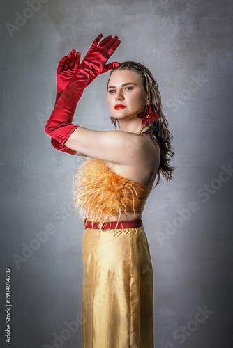 Portrait of a beautiful brunette with long hair in a golden evening dress with fur and red satin long gloves on her hands.
