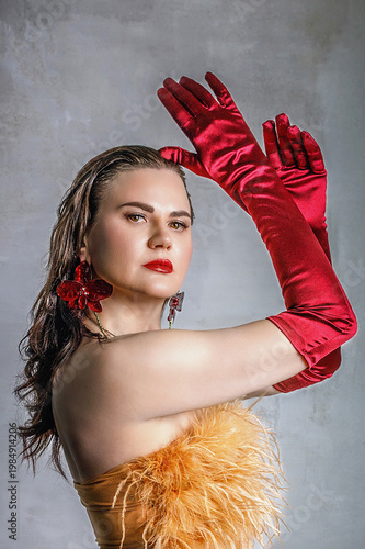 Portrait of a beautiful brunette with long hair in a golden evening dress with fur and red satin long gloves on her hands.