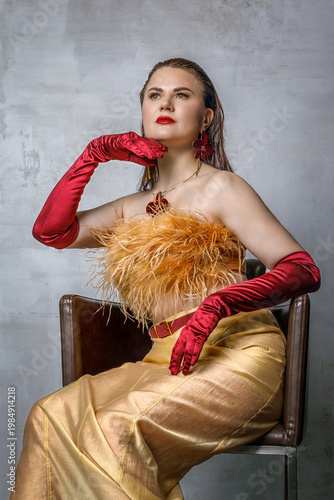 Portrait of a beautiful brunette with long hair in a golden evening dress with fur and red satin long gloves on her hands.