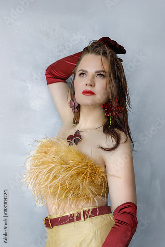 Portrait of a beautiful brunette with long hair in a golden evening dress with fur and red satin long gloves on her hands.