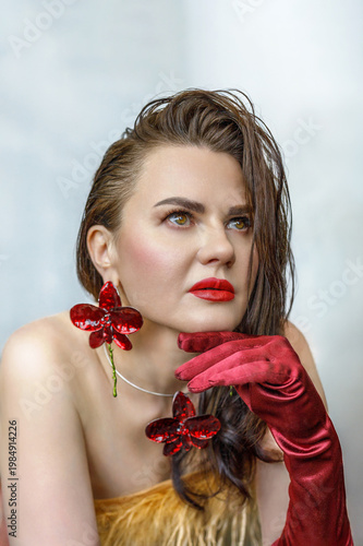 Portrait of a beautiful brunette with long hair in a golden evening dress with fur and red satin long gloves on her hands.