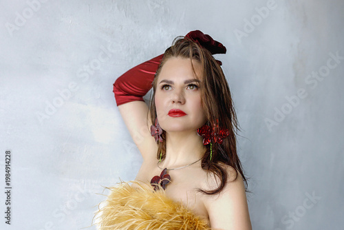 Portrait of a beautiful brunette with long hair in a golden evening dress with fur and red satin long gloves on her hands.