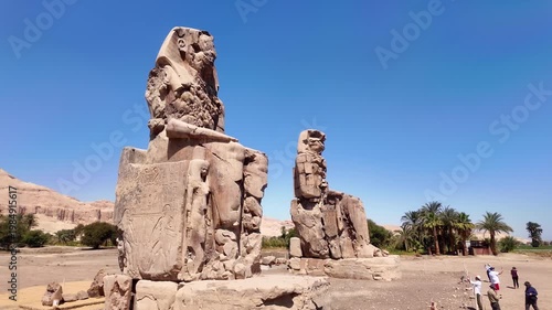 Horizontal panning shot moving left across tourists visiting the Colossi of Memnon statues in Luxor, Egypt. Cultural tourism and travel editorial concept.