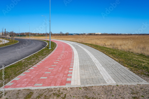 Konstfotografi Curving bike lane and sidewalk ending at open field with road and lampposts unde