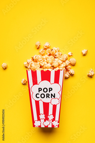 Popcorn with cheese taste in white and red cardboard bucket on bright yellow background top view.