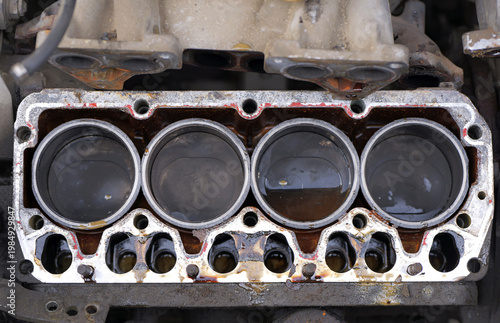 Four-cylinder engine block with removed cylinder head showing pistons, fluid contamination, and gasket residue, indicating maintenance and repair condition. 2026