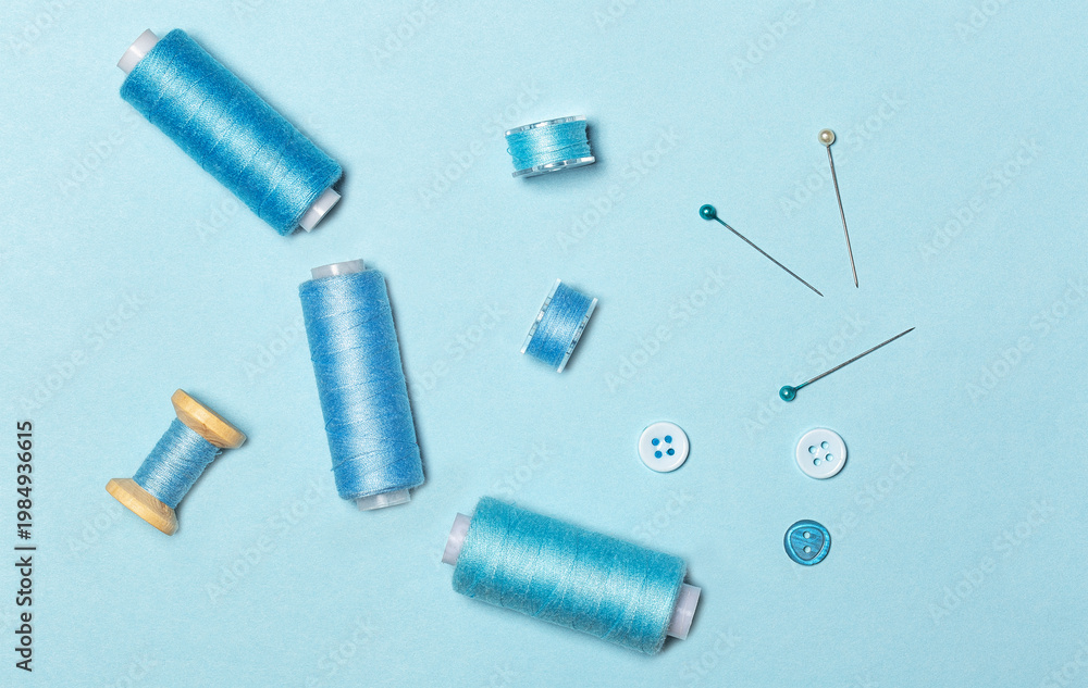 Fototapeta premium Sewing kit, blue threads on spools and sewing bobbins, buttons, top view.