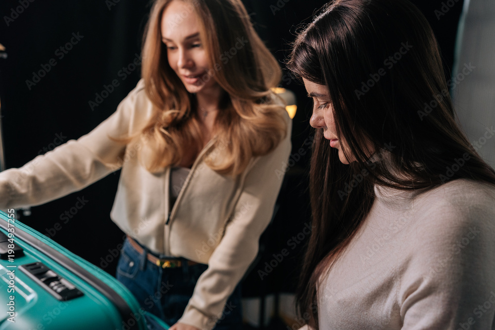 Fototapeta premium Two female friends checking suitcase, preparing for exciting journey, packing baggage for upcoming adventure and vacation planning. Concept of organization and travel essentials.