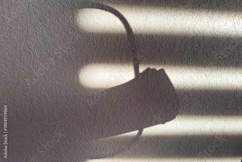 Shadows Create Shapes on a Wall as Light Filters Through Blinds in a Room During the Afternoon Hours, Showcasing a Hand Holding a Circle