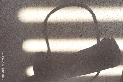 Light Creates a Shadow of a Bag on a Textured Wall During Daytime From Window Blinds