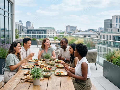 Diverse multi-ethnic group of friends and colleagues enjoying a healthy lunch together on a modern urban rooftop terrace with a city skyline view, laughing and sharing a meal in the sunshine