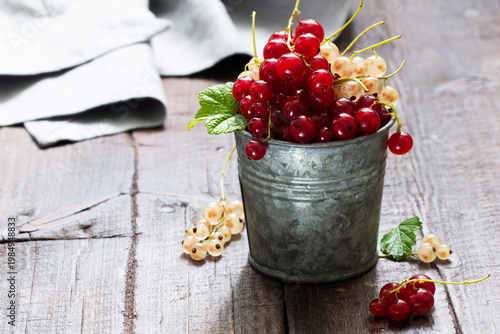 White and red currants in a metal bucket on a wooden background.