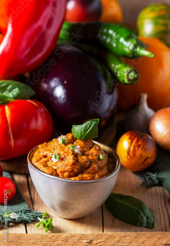 Eggplant caviar in a glass jar and vegetables on a wooden background.