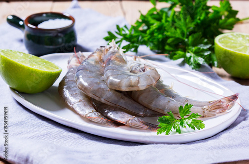 Fresh shrimp, lime, salt, and parsley on a ceramic plate on a wooden table.