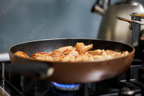 Frying small pieces of chicken meat in a pan on a gas stove