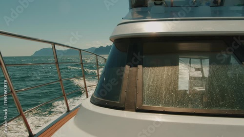 Yacht moves at high speed through sea bay leaving seething wake on water and silhouette of couple in cabin through glass.