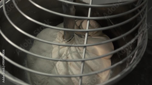 Mixing dough in a stainless steel bowl with a spiral mixer, showing the gradual incorporation of ingredients and the transformation of texture in a kitchen setting