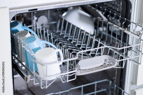 Open dishwasher with clean mugs and plates inside a modern home kitchen