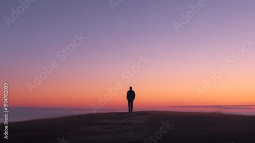 Lone figure silhouetted against a vast colorful sunrise sky from the crest of an open hill