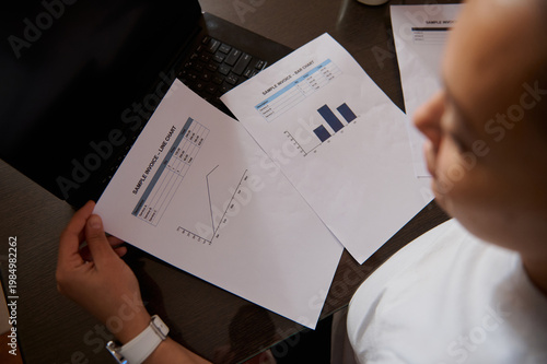 Photos Businesswoman Reviewing Financial Charts and Invoices at Laptop Desk