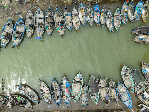 Aerial view of numerous boats, tightly packed along the Jepara Floating Fish Market's edge, create a textured mosaic on the water, Jepara, Central Java, Indonesia.