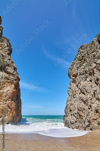 Scenic coastal gorge opening to a wild beach with crashing sea waves. Famous natural landmark in Europe for Mediterranean vacation advertising and travel brochures. Spectacular seaside scenery.