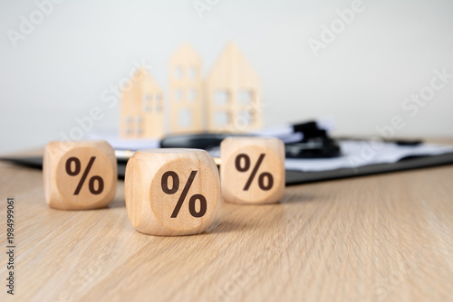 Percentage signs on wooden blocks. Blurred background with miniature houses and documents. Real estate interest rate concept.