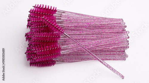 Close-up of pink glitter mascara wands and eyelash brushes on white background