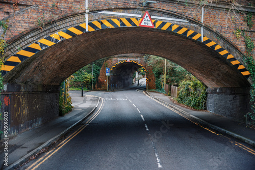 Empty Road Passing Under Brick Railway Bridge with Warning Markings