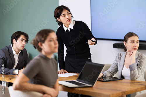 Confident young malaysian female student with remote control confidently took stage, ready to deliver impactful presentation to audience in light classroom