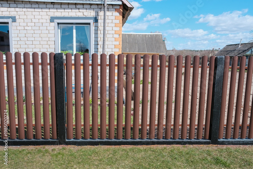 Modern brown metal euro fence panels home garden w section palisade picket with vertical slats and black posts. New privacy fencing, showcasing property boundary and residential security.