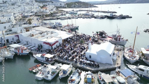 Aerial drone view of Easter celebration in Naousa village on Paros island, Greece, showing people gathered at outdoor tables in a festive Mediterranean atmosphere. Ideal for culture, travel, holidays