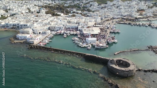 Aerial drone view of Easter celebration in Naousa village on Paros island, Greece, showing people gathered at outdoor tables in a festive Mediterranean atmosphere. Ideal for culture, travel, holidays