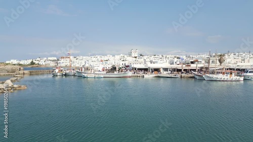 Aerial drone view of Naousa village on Paros island, Greece, showing traditional white buildings, coastal harbor and clear blue sea in daylight. Ideal for travel, tourism and Mediterranean lifestyle 