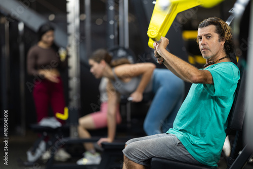 Canvas Print Adult man doing strength exercises on his shoulders while sitting in a press machine