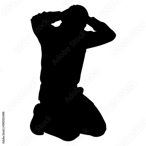 Silhouette of a man kneeling with hands on head.