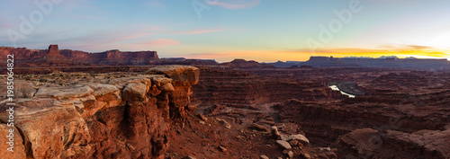 This scenic panorama of Canyonlands National Park near Moab, Utah, features Buck Canyon with a glimpse of the Colorado River underneath a colorful sky at dawn.