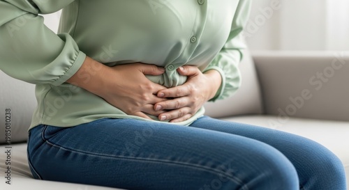 Woman experiences severe abdominal pain while sitting on a couch.