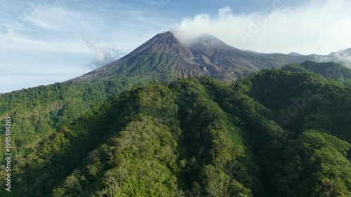 A tropical wilderness with mighty volcanic mountains and dense forest canopies under gentle sunlight. Mount Merapi National Park in Indonesia.