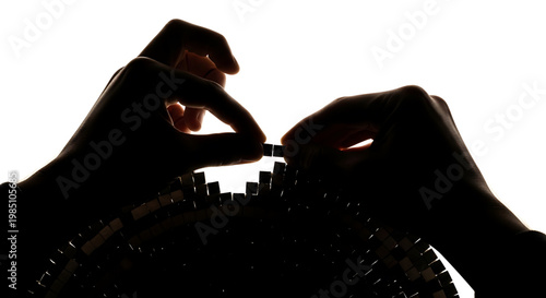 A person's hands carefully placing a domino in a delicate chain of falling dominos in a silhouette against a white background
